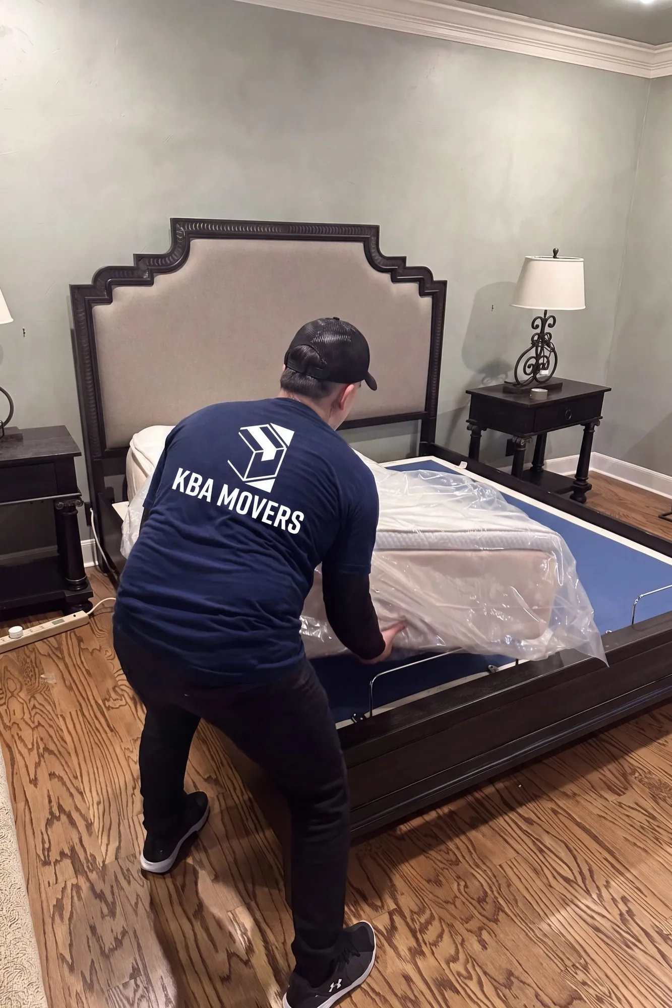 Mover wrapping a bed frame in protective plastic in a bedroom