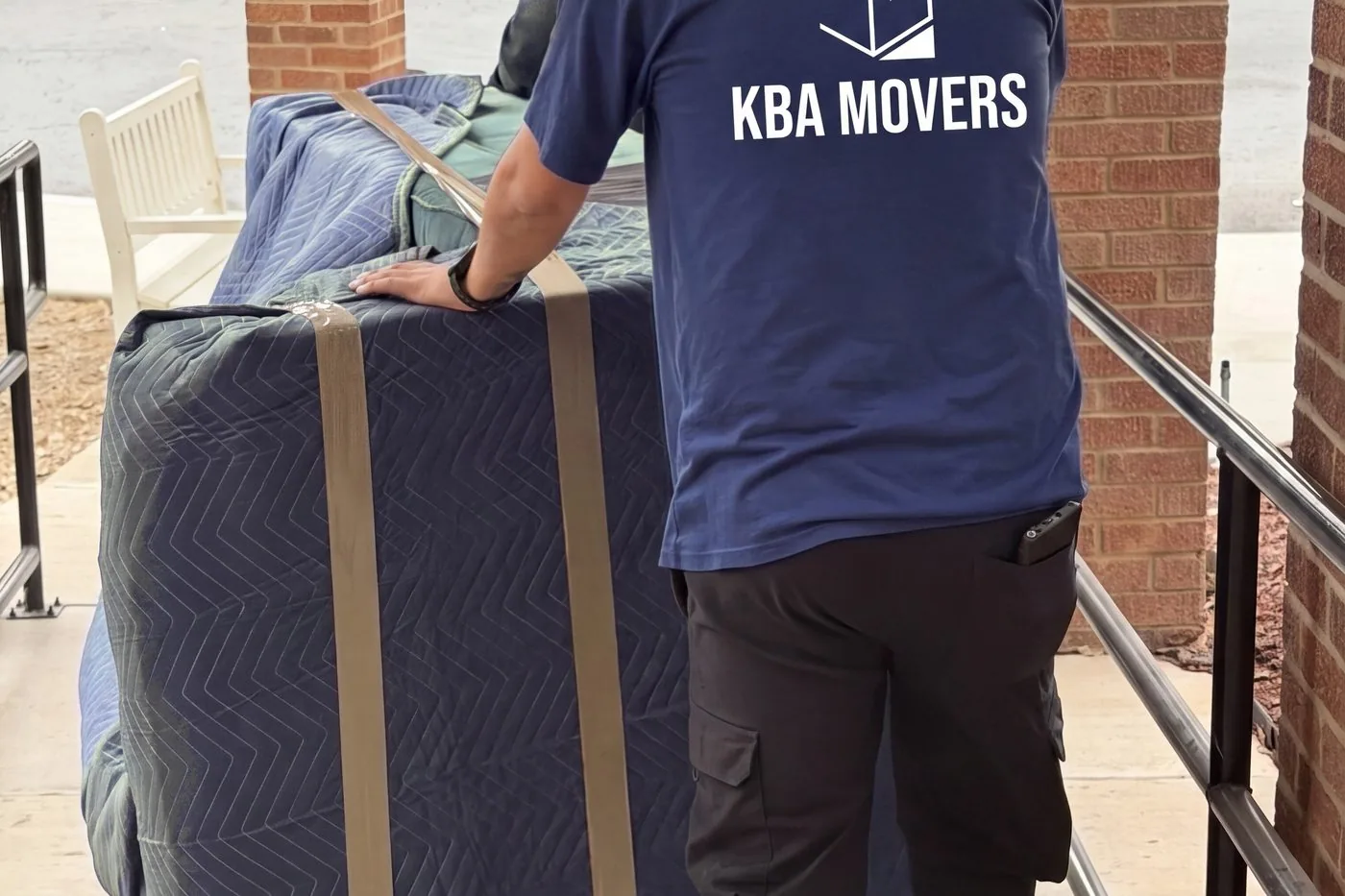Mover wheeling a blanket-wrapped mattress along a covered walkway