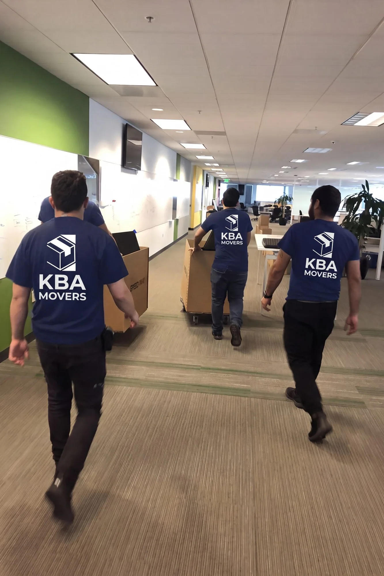 Crew carrying boxes and a dolly through an office corridor during a workplace move