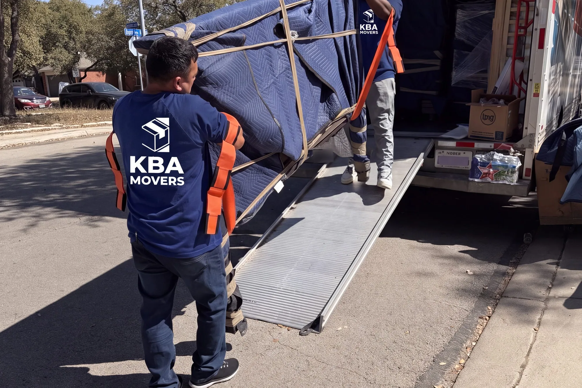 Movers wheeling a blanket-wrapped item down a truck ramp