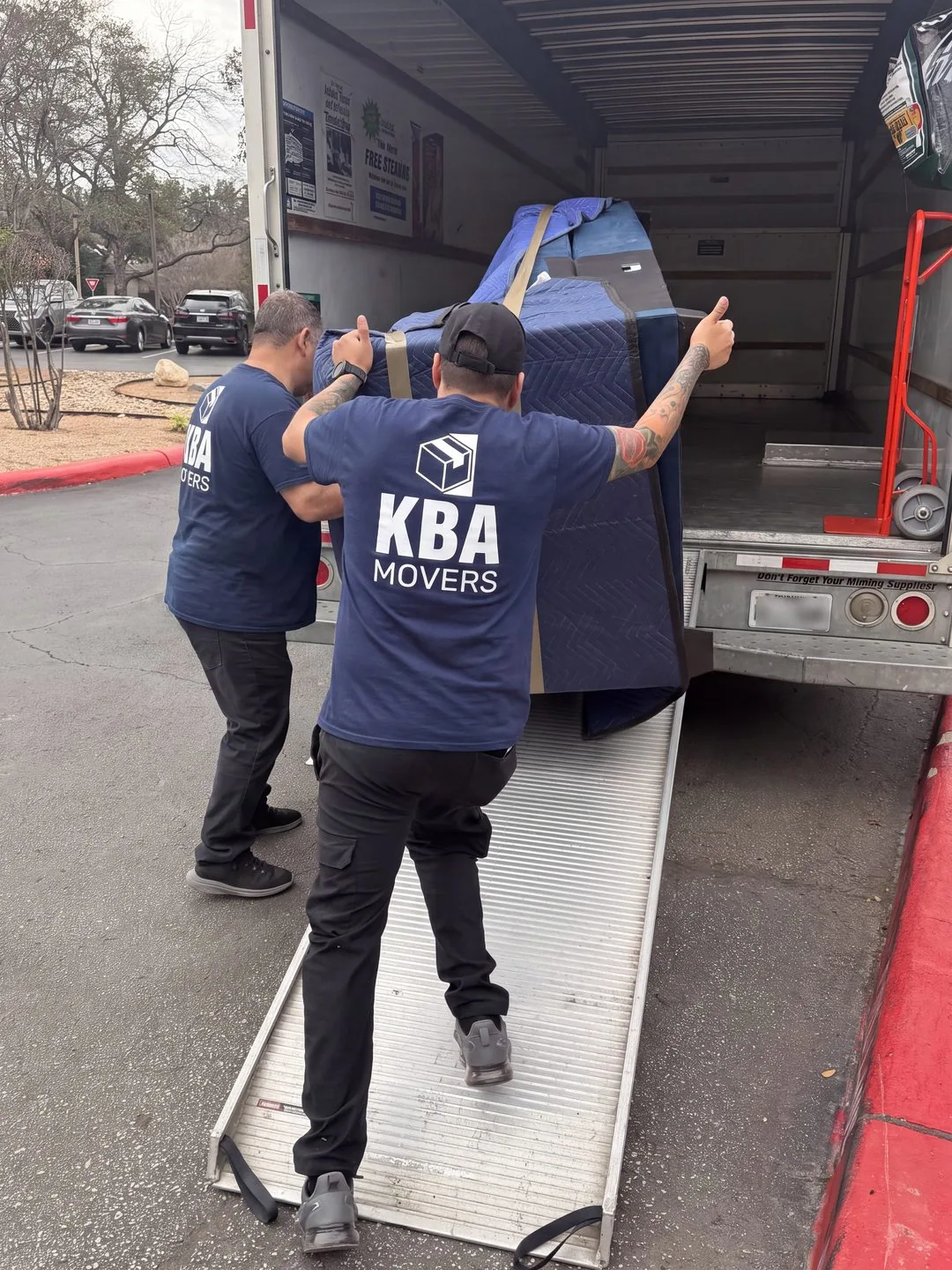 Movers carrying a blanket-wrapped sofa up the ramp into a moving truck
