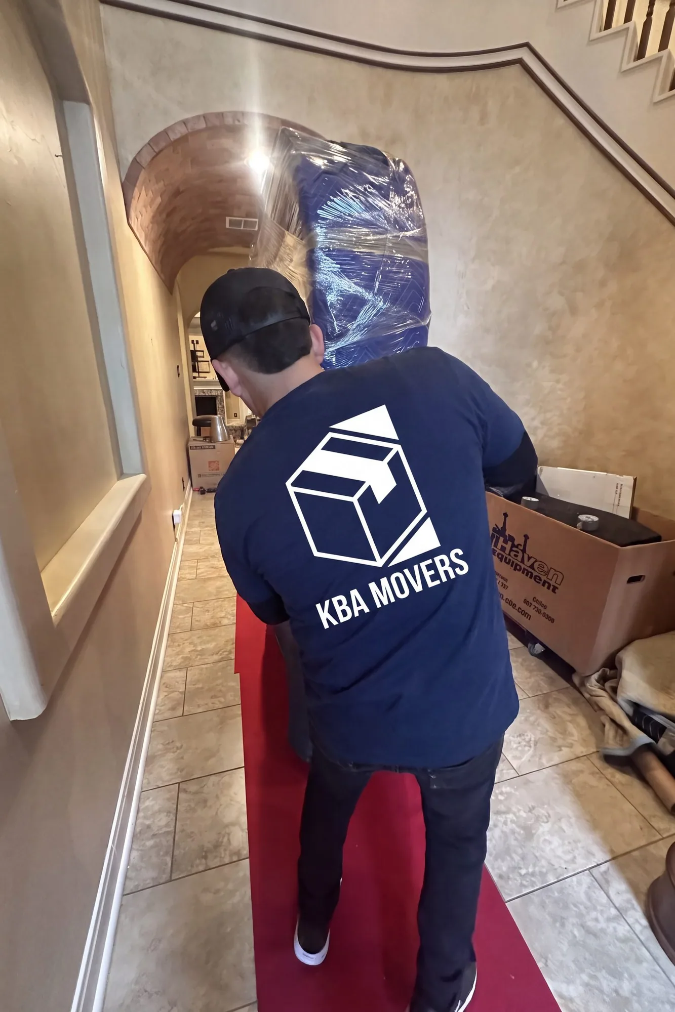 Mover carrying a wrapped item up a staircase inside a home